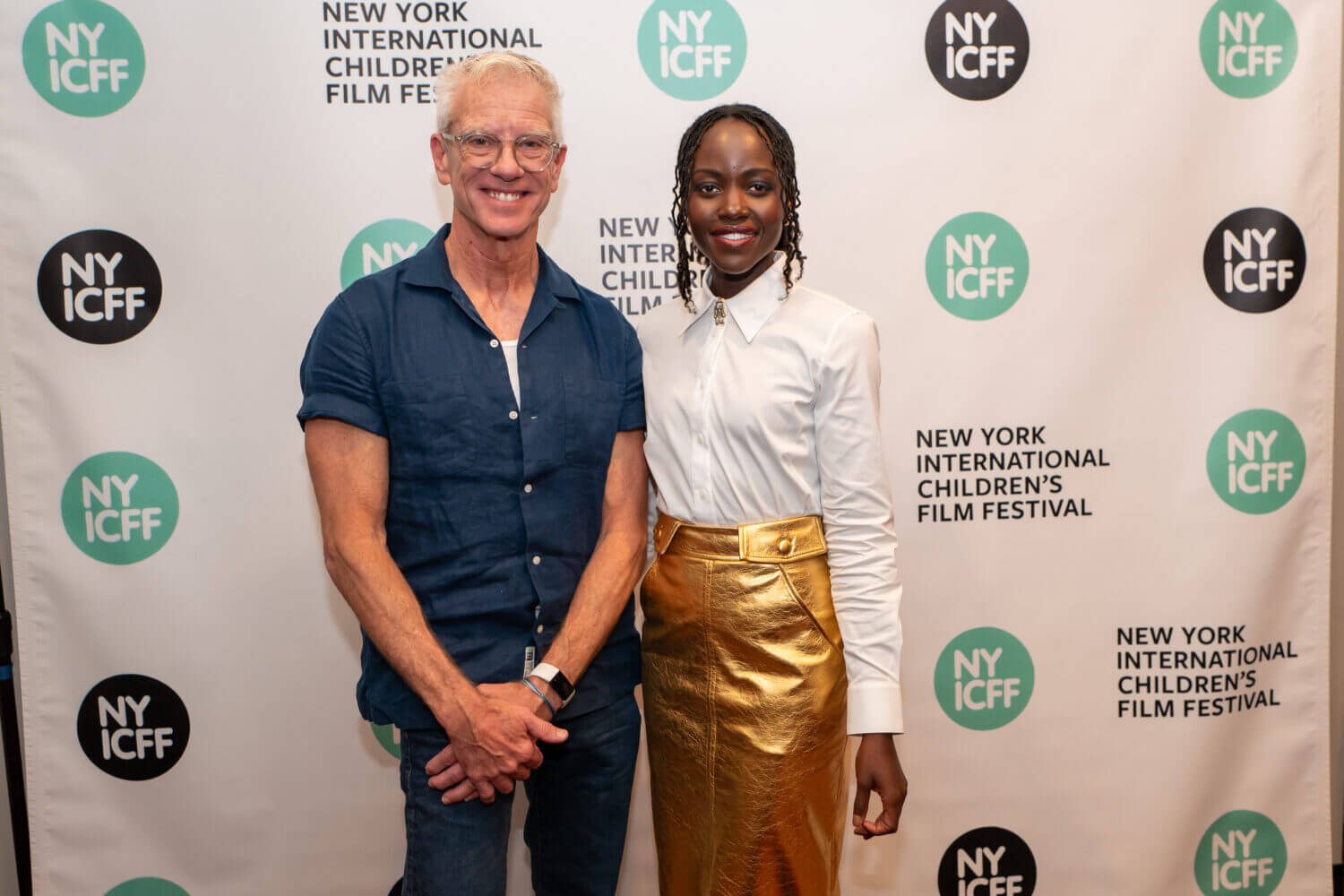 Lupita Nyong'o and Chris Sanders pose in front of a NYICFF banner