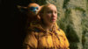 A young girl in a yellow raincoat stares in awe while a small creature sits on her shoulder